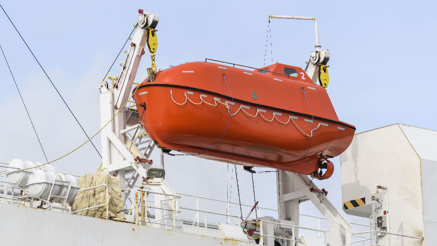 Lifeboat on big cargo vessel. Lowering orange lifeboat to water.